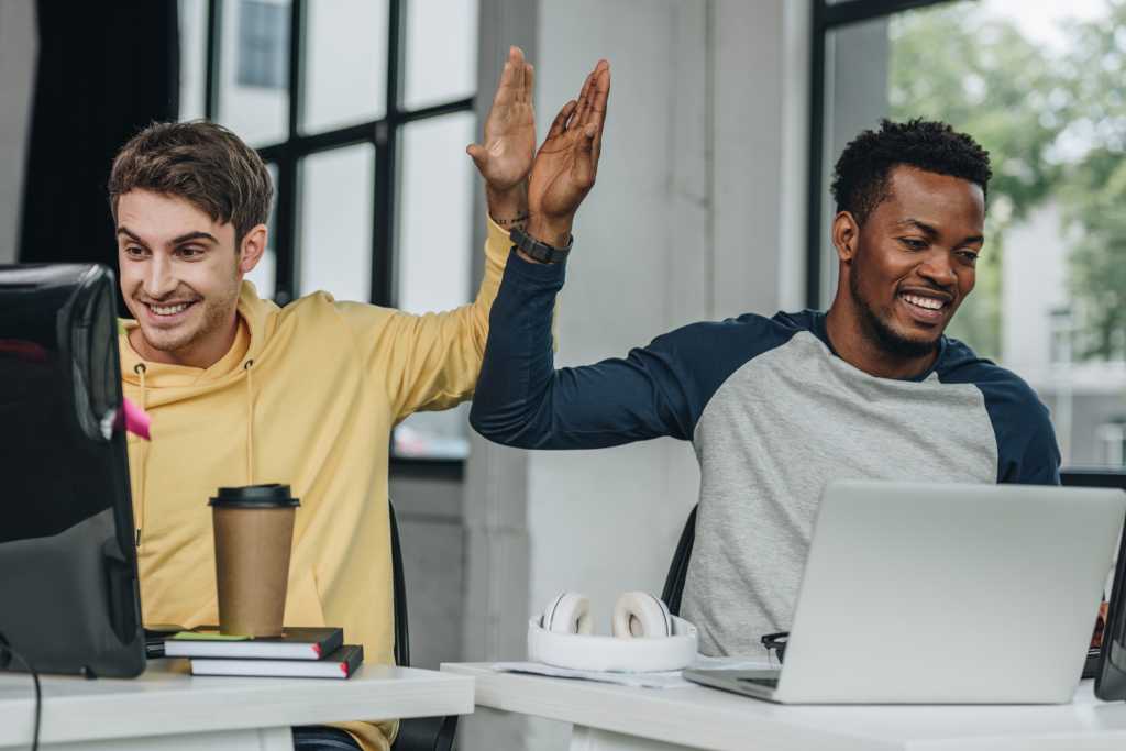 happy multicultural programmers developers giving high five while working in office together